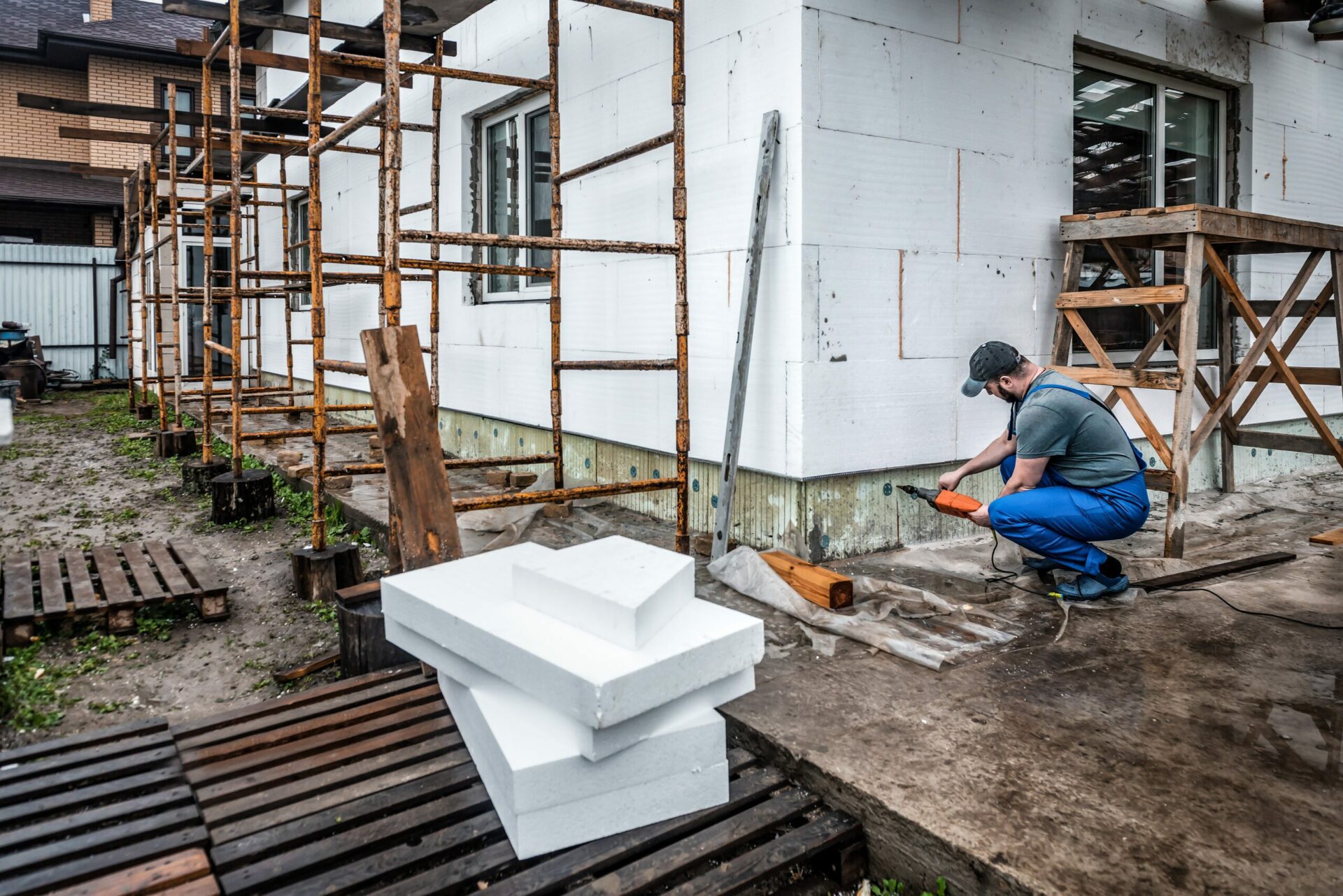 Worker is drilling holes to fix the styrofoam board on the facade. Insulation of the house with polyfoam